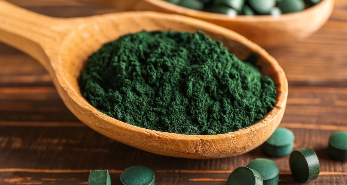 Cuillère de poudre de spiruline et pilules sur une table en bois