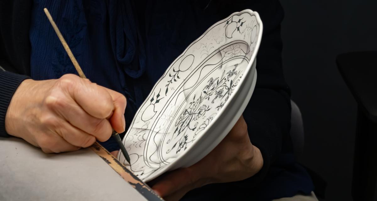 Une dame en train de calligraphier une assiette en porcelaine, pour un cadeau classique mais significatif.