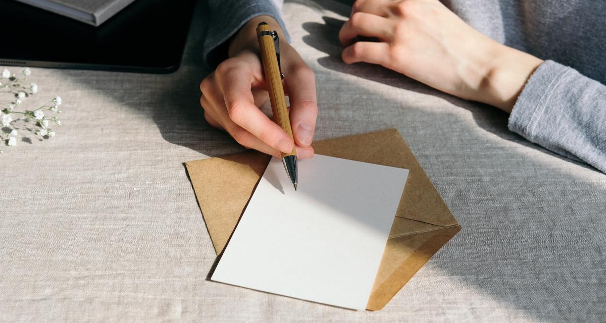 Une femme s'apprête à écrire un mot sur une carte, avant de la glisser dans une enveloppe.