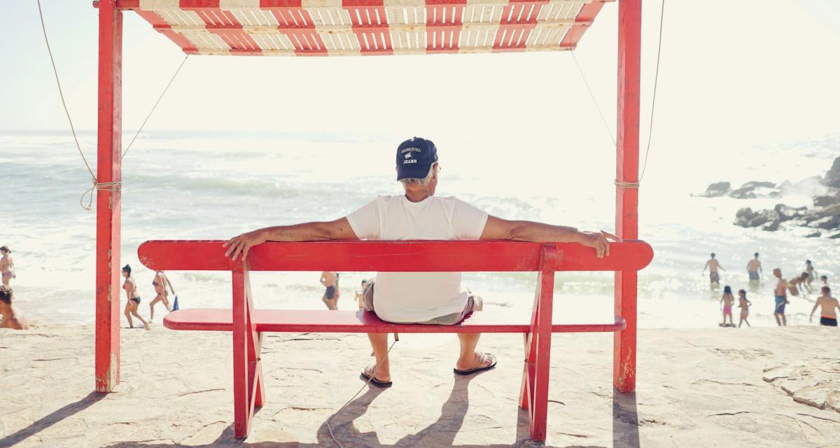 Un homme aux cheveux blancs assis sur un banc près de la plage.