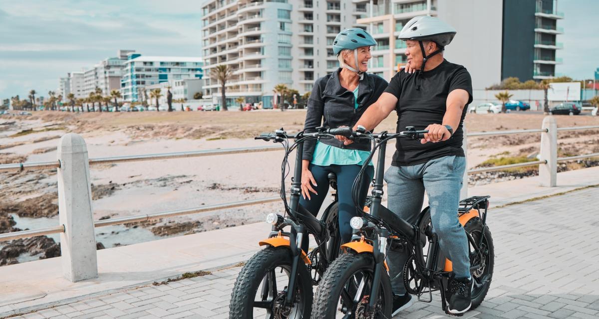 Un couple de senior se balade en vélo électrique dans une station balnéaire.