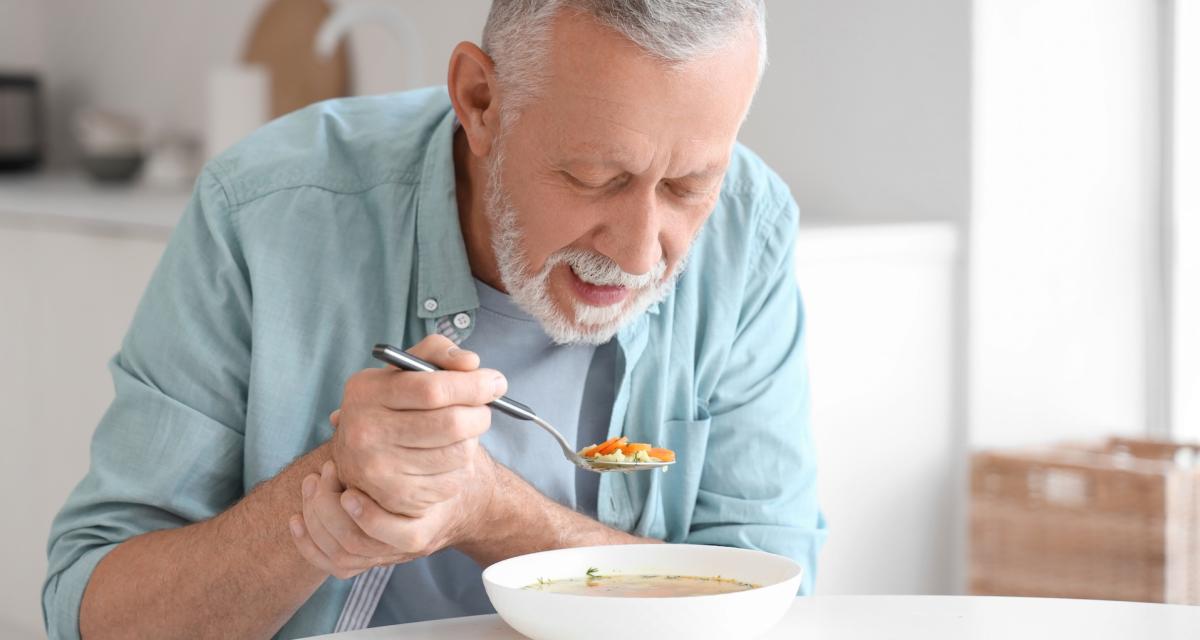 Un senior doit contrôler les tremblements de sa main, alors qu'il mange.