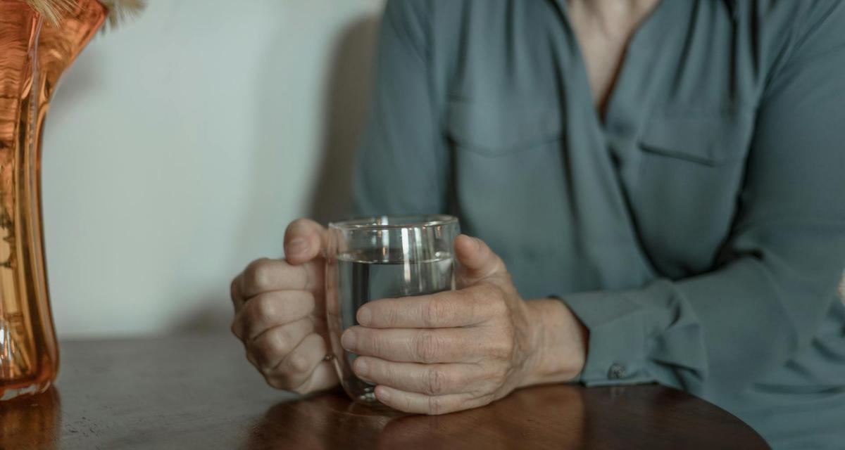 Une femme relativement âgée tient un verre d'eau rempli dans ses mains?