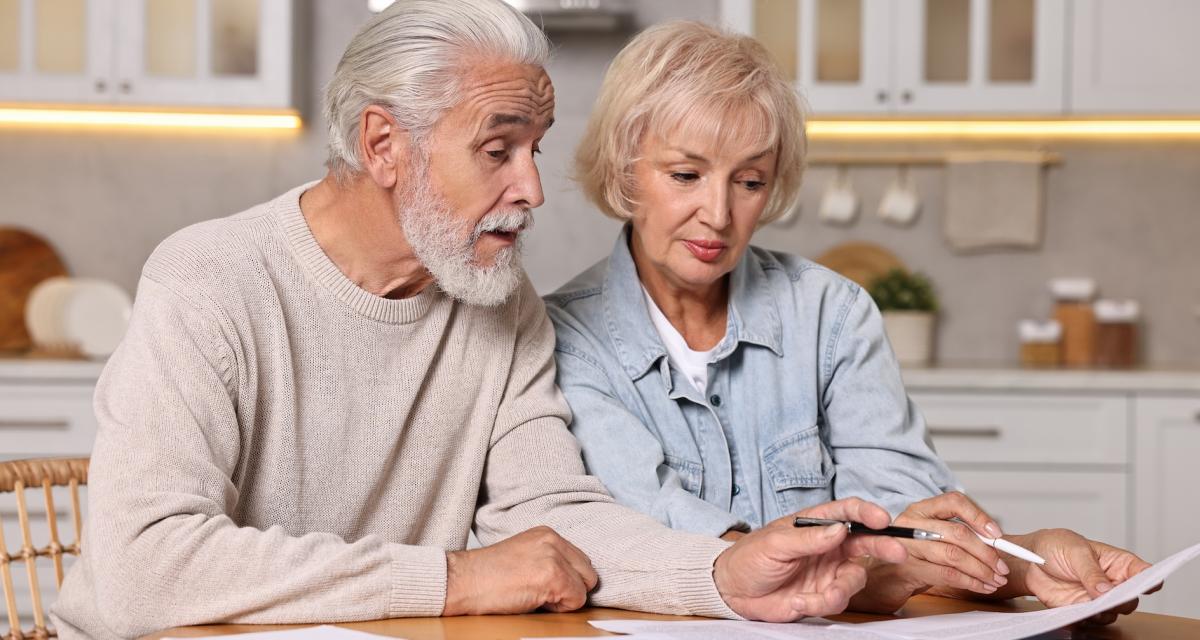 Un couple de seniors lisent des documents au sujet de la retraite et des nombres de trimestres cotisés.