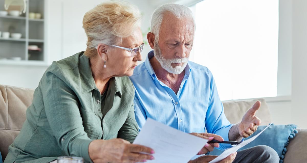 Un couple âgé regarde attentivement les documents liés au décès d'un co-titulaire de leur compte joint.