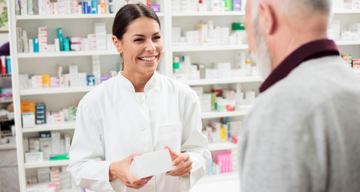 Une pharmacienne tend une boite de médicaments à un patient.