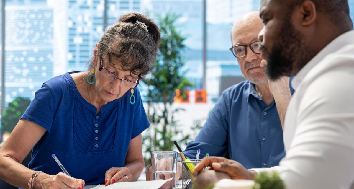 Un couple de seniors signent un contrat de mutuelle ou de prévoyance à l'issue d'un rendez-vous avec un conseiller.