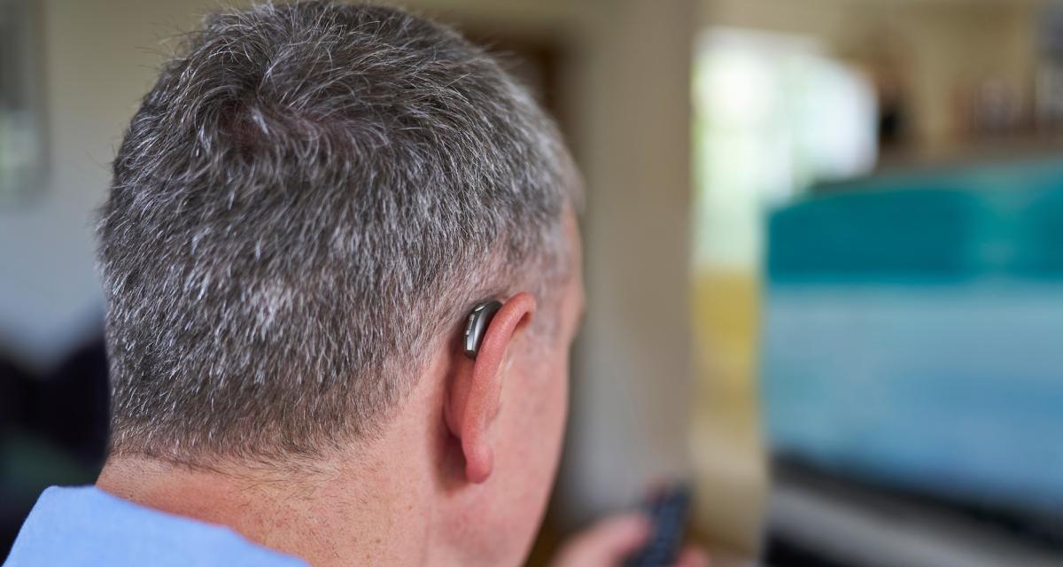 Un homme porte une prothèse auditive pour ses tâches quotidiennes (comme regarder la télévision).