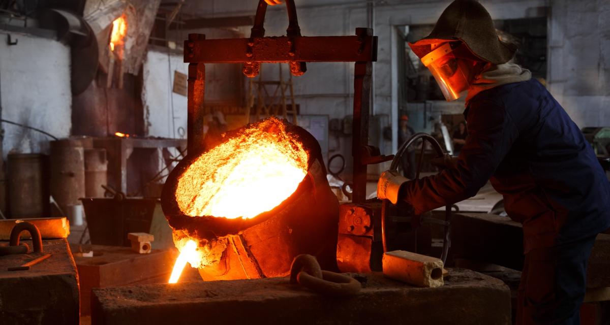 Un travailleur industriel en tenue de protection verse du métal fondu à la fonderie d'acier, qui pourra utiliser ses points de pénibilité. 