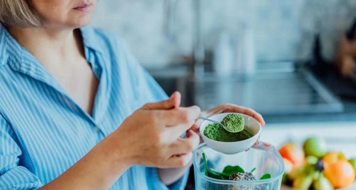 Une femme ajoute une cuillère de poudre de spiruline dans son mixeur.