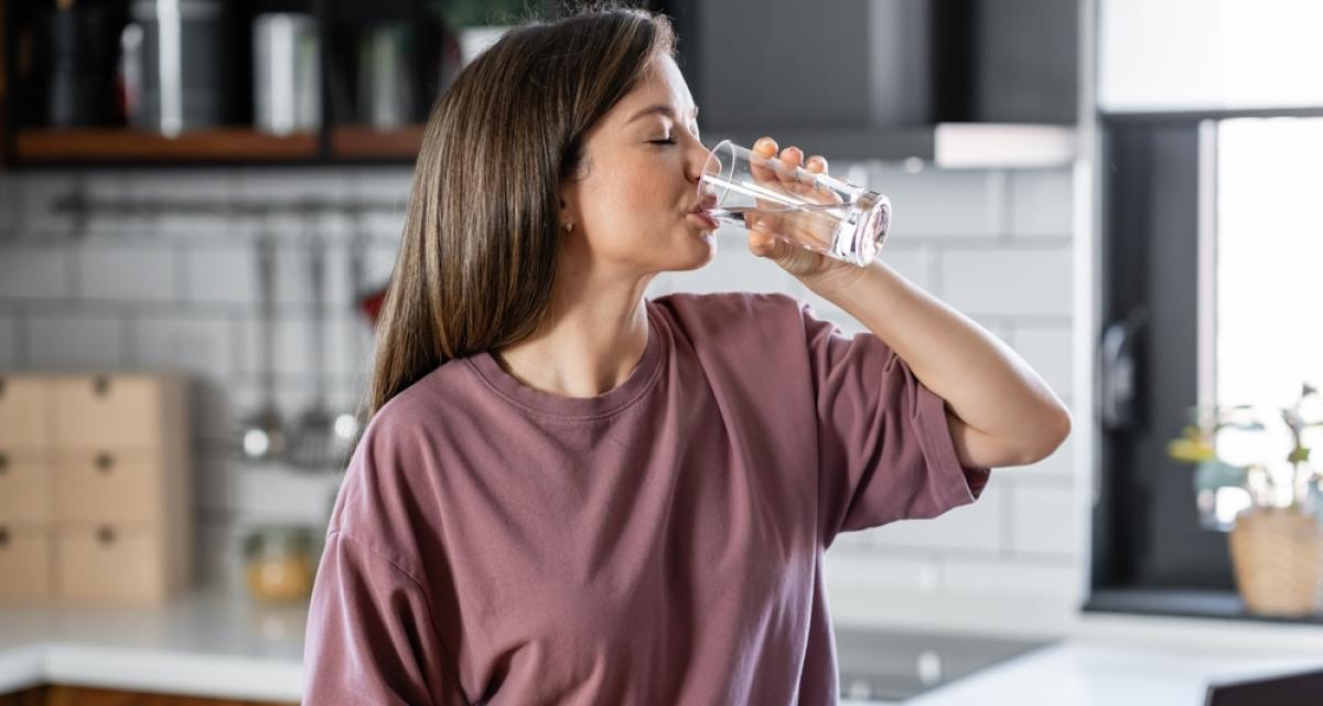 Une femme, qui a tout le temps soif, est en train de boire un verre d'eau.