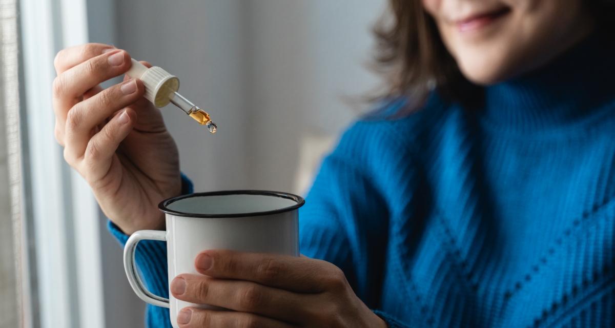 Une femme en train de mettre des gouttes de CBD dans sa tasse de thé.